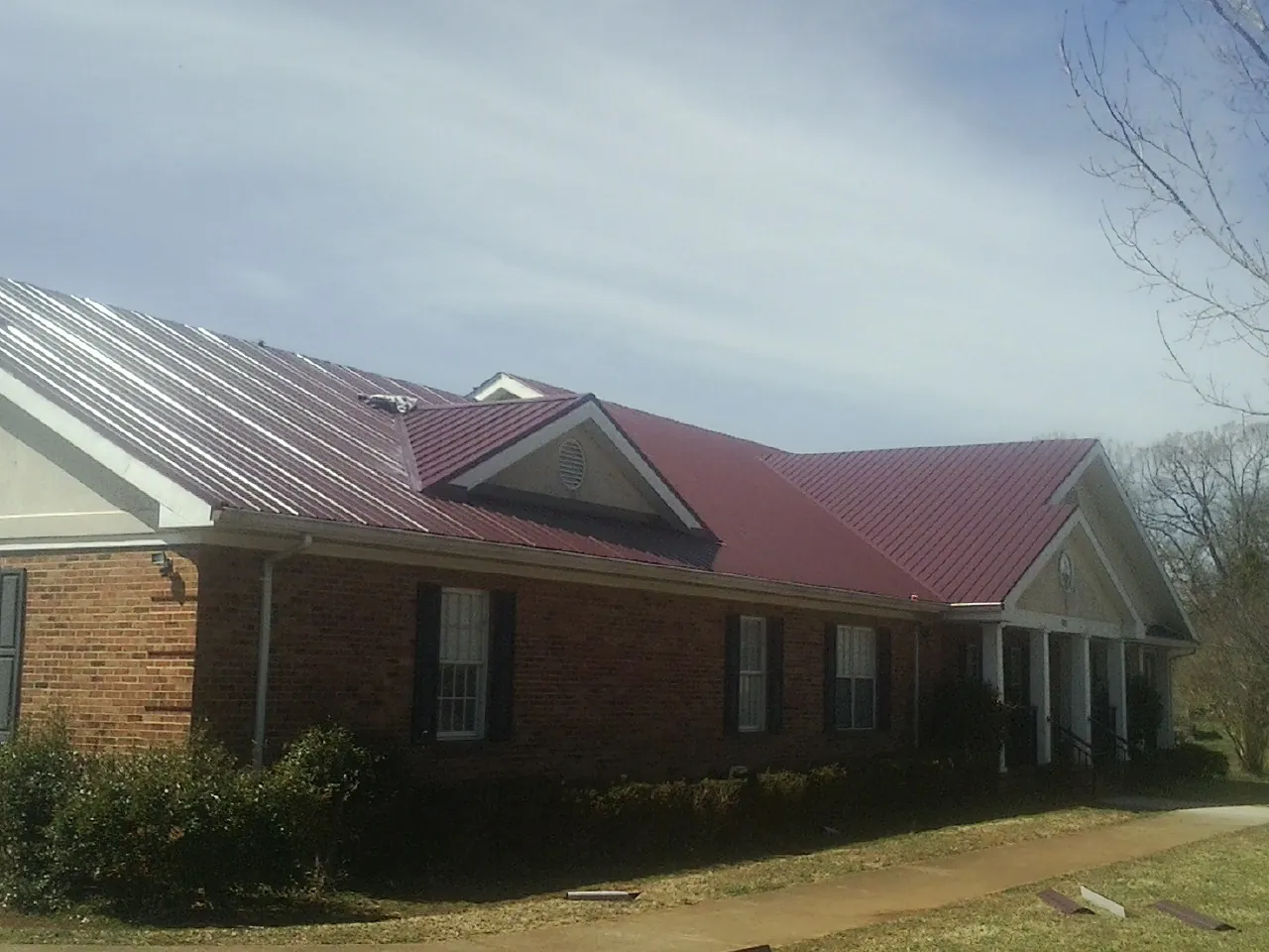 Red metal roof with gabled entries on a long brick building, from a Hail Damage Roof Repair job in Lane